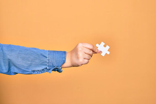 Hand of caucasian young woman holding piece of puzzle over isolated yellow background