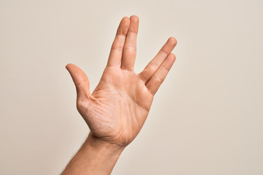 Hand of caucasian young man showing fingers over isolated white background greeting doing Vulcan salute, showing hand palm and fingers, freak culture