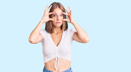 Young beautiful blonde woman wearing casual white tshirt trying to open eyes with fingers, sleepy and tired for morning fatigue