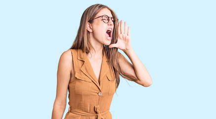 Young beautiful blonde woman wearing casual clothes and glasses shouting and screaming loud to side with hand on mouth. communication concept.