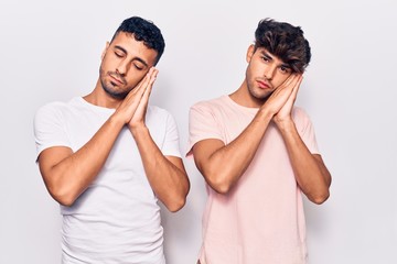 Young gay couple wearing casual clothes sleeping tired dreaming and posing with hands together while smiling with closed eyes.