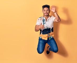Fototapeta na wymiar Young handsome latin man wearing casual clothes smiling happy. Jumping with smile on face doing ok sign with thumbs up over isolated yellow background
