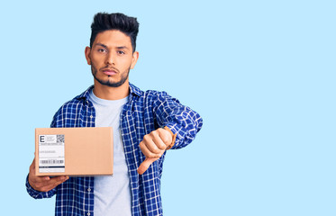 Handsome latin american young man holding delivery package with angry face, negative sign showing dislike with thumbs down, rejection concept