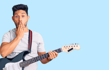Obraz premium Handsome latin american young man playing electric guitar covering mouth with hand, shocked and afraid for mistake. surprised expression
