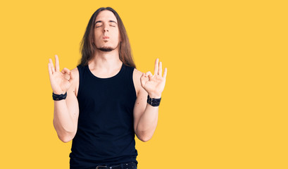 Young adult man with long hair wearing goth style with black clothes relaxed and smiling with eyes closed doing meditation gesture with fingers. yoga concept.