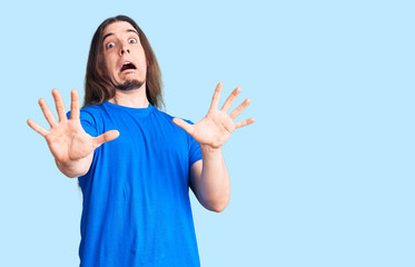 Young adult man with long hair wearing swimwear afraid and terrified with fear expression stop gesture with hands, shouting in shock. panic concept.