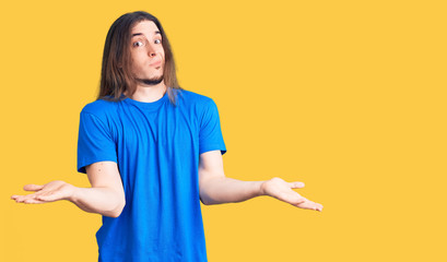 Young adult man with long hair wearing swimwear clueless and confused expression with arms and...