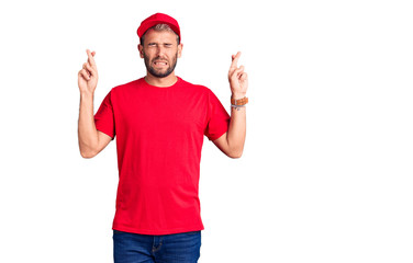 Naklejka premium Young handsome blond man wearing t-shirt and cap gesturing finger crossed smiling with hope and eyes closed. luck and superstitious concept.