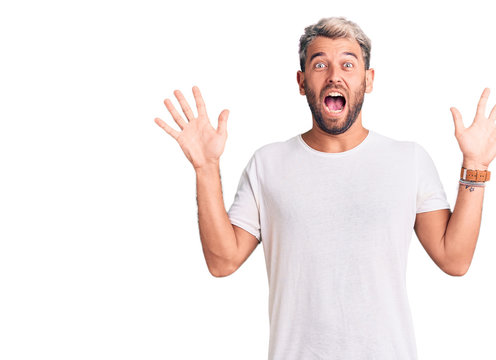 Young handsome blond man wearing casual t-shirt pointing fingers to camera with happy and funny face. good energy and vibes.