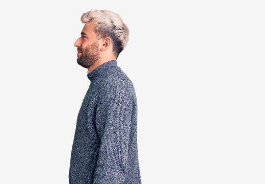 Young handsome blond man wearing casual sweater looking to side, relax profile pose with natural face with confident smile.