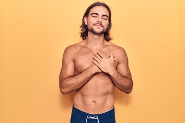 Young handsome man wearing swimwear shirtless smiling with hands on chest, eyes closed with grateful gesture on face. health concept.