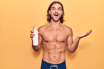 Fototapeta premium Young handsome man wearing swimwear holding sunscreen lotion celebrating achievement with happy smile and winner expression with raised hand