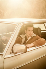 A handsome man driving an oldtimer car travels into the sunset