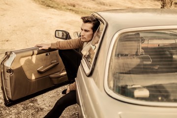 A handsome man driving an oldtimer car travels into the sunset