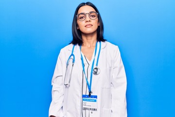 Young beautiful latin woman wearing doctor stethoscope and id card with serious expression on face....