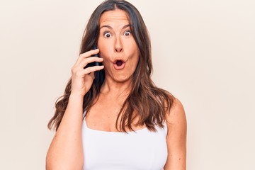 Fototapeta premium Beautiful brunette woman having conversation talking on the smartphone over white background scared and amazed with open mouth for surprise, disbelief face