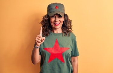 Middle age brunette woman wearing t-shirt and cap with red star symbol of communism smiling with an idea or question pointing finger up with happy face, number one
