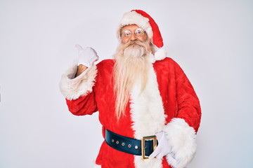 Old senior man with grey hair and long beard wearing santa claus costume smiling with happy face looking and pointing to the side with thumb up.
