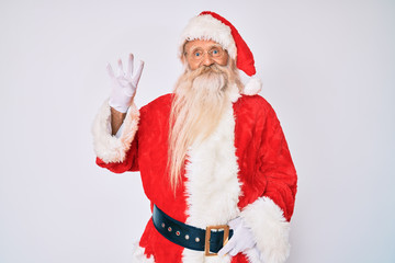 Old senior man with grey hair and long beard wearing santa claus costume with suspenders showing and pointing up with fingers number four while smiling confident and happy.