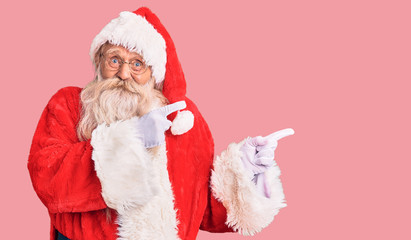 Old senior man with grey hair and long beard wearing traditional santa claus costume pointing aside worried and nervous with both hands, concerned and surprised expression