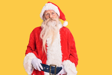 Old senior man with grey hair and long beard wearing traditional santa claus costume relaxed with serious expression on face. simple and natural looking at the camera.