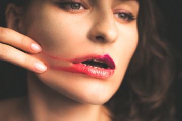 Portrait of a girl smearing lipstick on her face with her manicured fingers