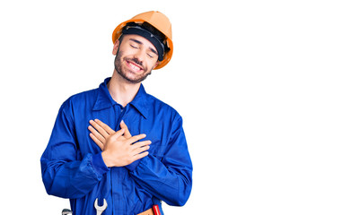 Young hispanic man wearing worker uniform smiling with hands on chest with closed eyes and grateful gesture on face. health concept.