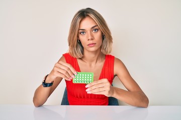 Beautiful caucasian woman holding birth control pills thinking attitude and sober expression...