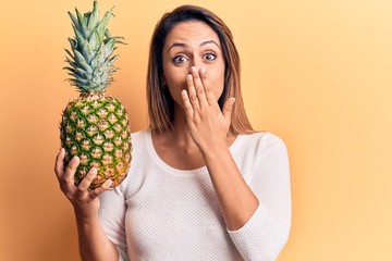 Young beautiful woman holding pineapple covering mouth with hand, shocked and afraid for mistake....