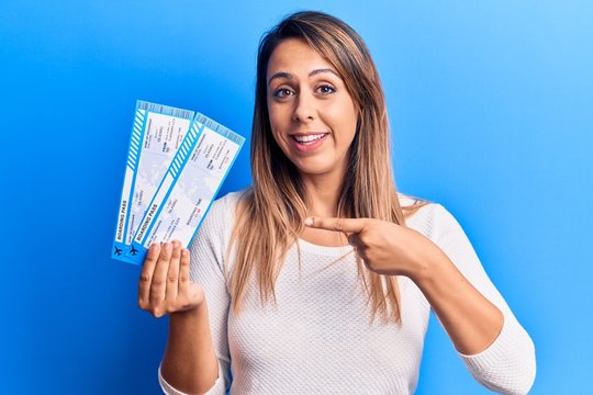Young beautiful woman holding airline boarding pass smiling happy pointing with hand and finger
