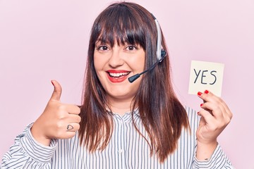 Young plus size woman wearing call center agent headset holding yes reminder smiling happy and...