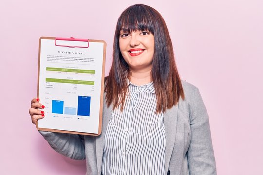 Young plus size woman holding clipboard with chart information paper looking positive and happy standing and smiling with a confident smile showing teeth