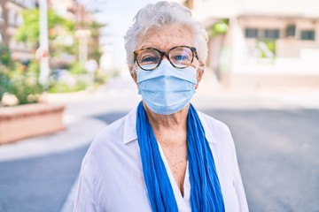 Elder senior woman with grey hair wearing coronavirus safety mask outdoors