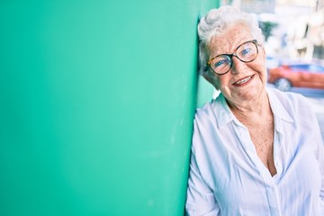 Elder senior woman with grey hair smiling happy leaning on the wall outdoors