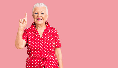 Senior beautiful woman with blue eyes and grey hair wearing a red summer dress showing and pointing up with finger number one while smiling confident and happy.