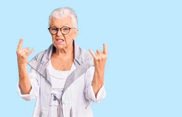 Senior beautiful woman with blue eyes and grey hair wearing casual clothes and glasses shouting with crazy expression doing rock symbol with hands up. music star. heavy concept.
