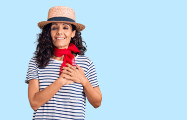 Middle age beautiful woman wearing casual striped t shirt and summer hat smiling with hands on chest with closed eyes and grateful gesture on face. health concept.