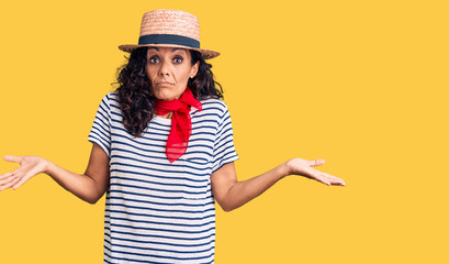 Middle age beautiful woman wearing casual striped t shirt and summer hat clueless and confused...