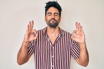 Naklejka premium Handsome hispanic man with beard wearing casual clothes relax and smiling with eyes closed doing meditation gesture with fingers. yoga concept.