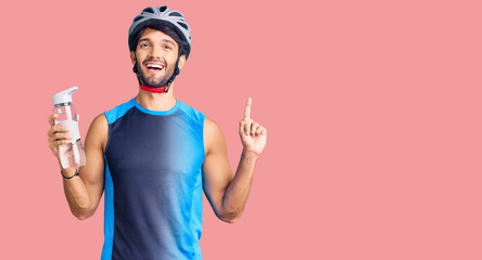 Handsome hispanic man wearing bike helmet and holding water bottle surprised with an idea or question pointing finger with happy face, number one