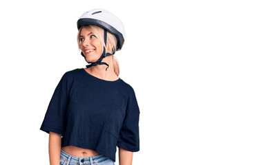 Young beautiful blonde woman wearing bike helmet looking away to side with smile on face, natural expression. laughing confident.