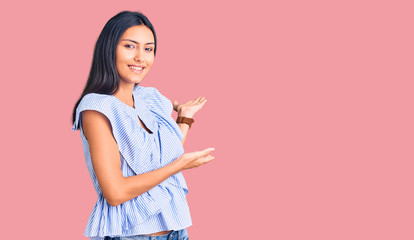 Young beautiful latin girl wearing casual clothes inviting to enter smiling natural with open hand