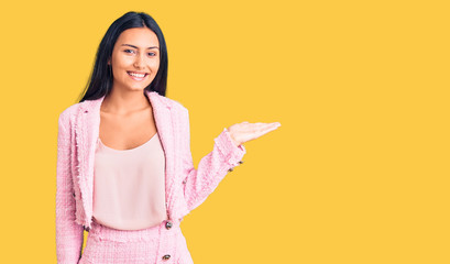 Young beautiful latin girl wearing business clothes smiling cheerful presenting and pointing with palm of hand looking at the camera.
