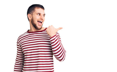 Naklejka premium Young handsome man wearing striped sweater smiling with happy face looking and pointing to the side with thumb up.