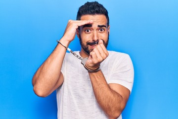 Young hispanic man wearing prisoner handcuffs stressed and frustrated with hand on head, surprised...
