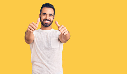 Young hispanic man wearing casual clothes approving doing positive gesture with hand, thumbs up...