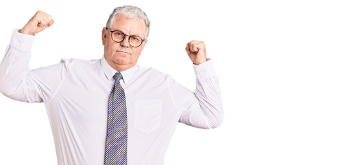 Senior grey-haired man wearing business clothes showing arms muscles smiling proud. fitness concept.
