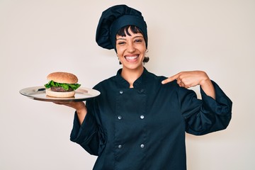 Beautiful brunettte woman chef holding burguer pointing finger to one self smiling happy and proud