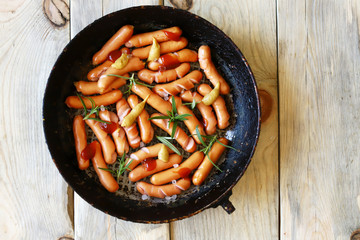 Appetizing fried mini sausages in a pan. Organic sausages. Rustic style.