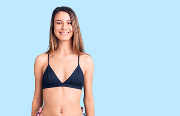 Young beautiful girl wearing bikini looking positive and happy standing and smiling with a confident smile showing teeth